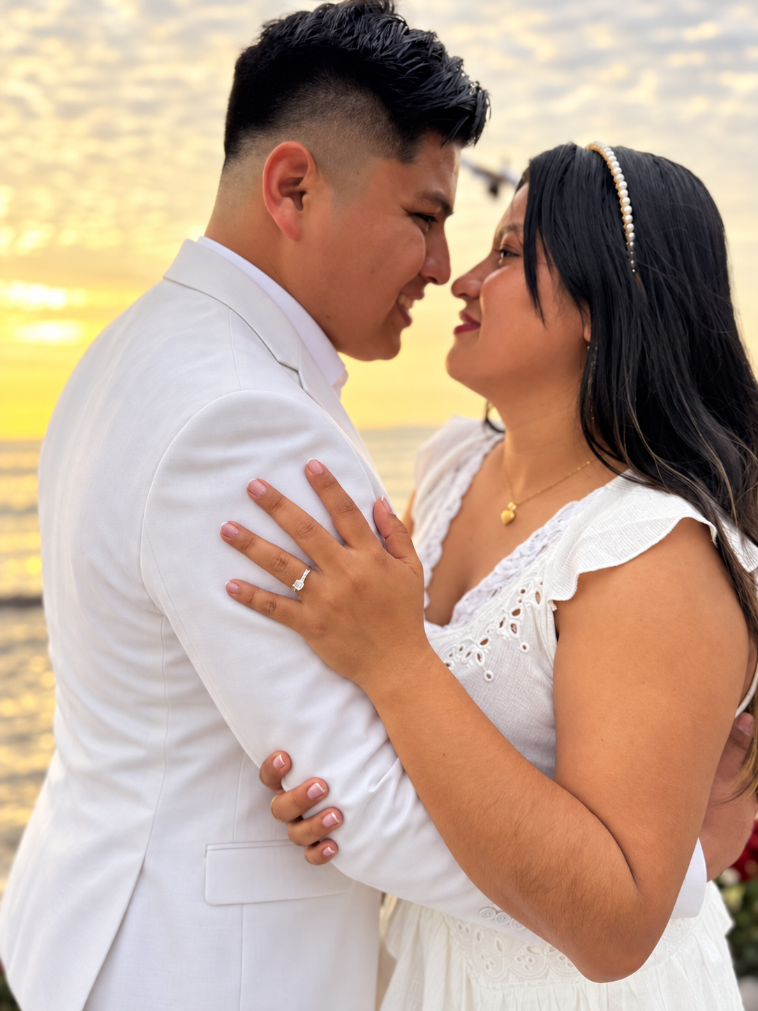 Marvin y Leydi abrazados frente al mar; Marvin viste un traje blanco